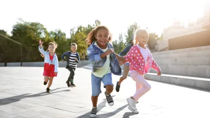 Group of five small children running on concrete outdoors on sunny day.